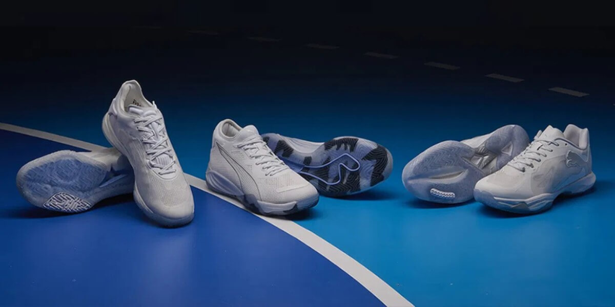 Trei perechi de pantofi de handbal Puma pe un teren de handbal albastru